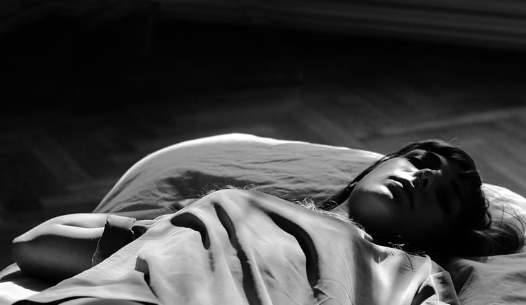 Black and white photo of young woman asleep on her back in bed