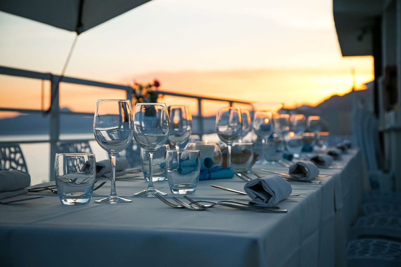 Long dinner table set for dining outdoors with sunset in the background