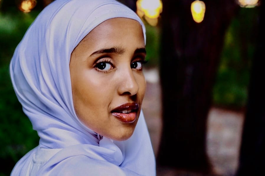 Closeup of young Somalian woman in lavender hijab as looks over her shoulder with sunset and trees in background