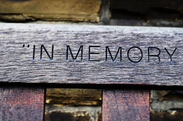 Closeup of wooden bench with the words in memory engraved on the backrest