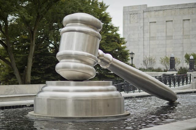 Silver gavel statue in shallow pool of water outside of courthouse building