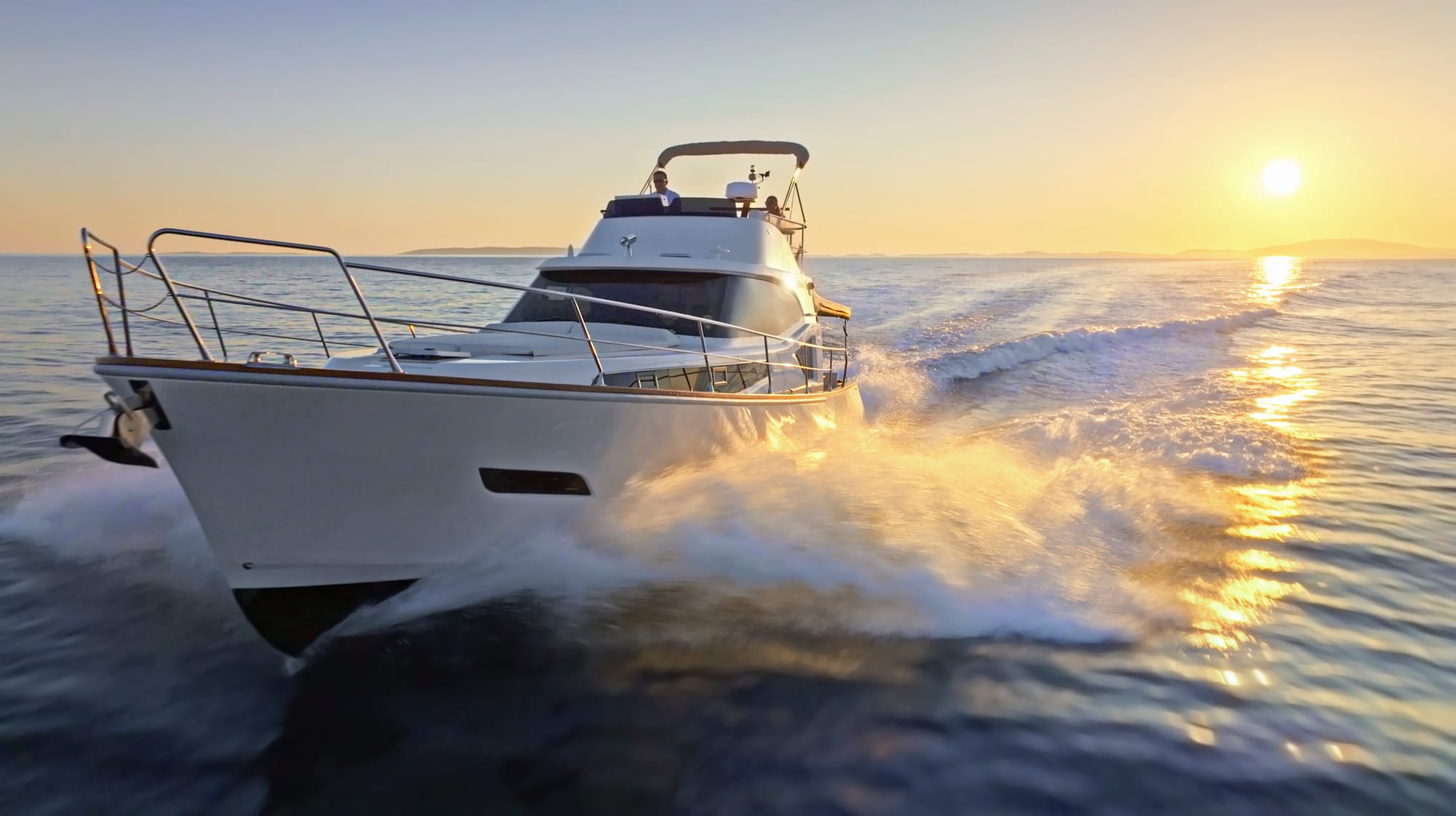 Cabin cruiser boat sailing through the water with sun low on the horizon in the background