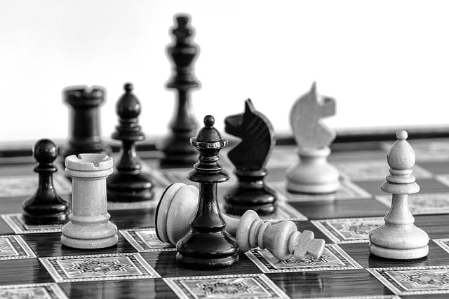 Black and white photo of chess board with chess pieces, one is tipped over on its side