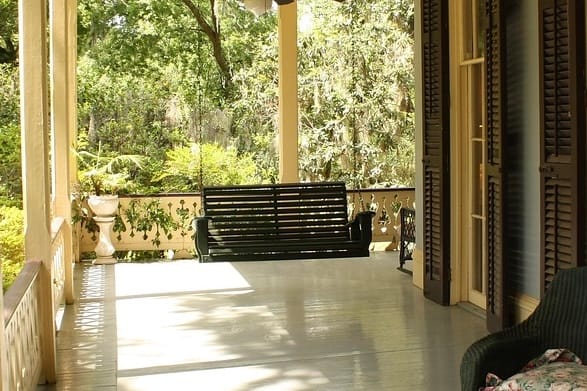 Porch swing on porch of blue home with black shutters